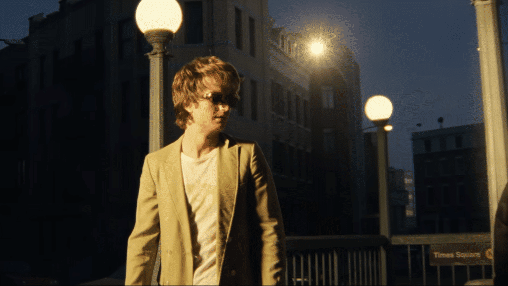 Joe Keery stands on a darkened street with sunglasses on.